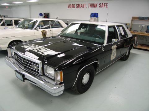 1991 Ford LTD Crown Victoria - black-over-white police cruiser numbered 45 with POLICE on the hood, photographed under a Work Smart Think Safe wall sign.