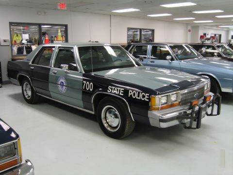 1991 Ford LTD Crown Victoria - Front quarter view of a two-tone green State Police sedan numbered 700 with a door emblem and chrome push bar indoors.