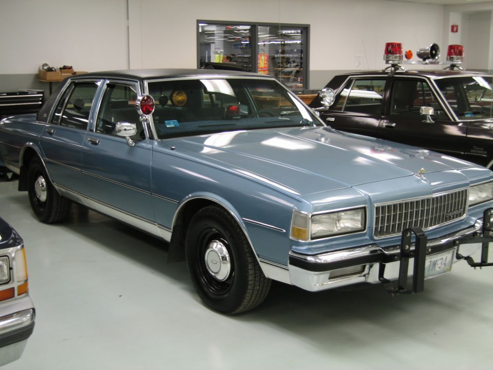 Light blue 1980s Chevrolet Caprice sedan with spotlight and push bar indoors