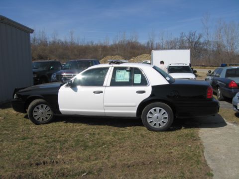 1991 Ford LTD Crown Victoria - Side profile of a black-and-white Ford Crown Victoria police sedan with a roof light bar, parked on grass outdoors.