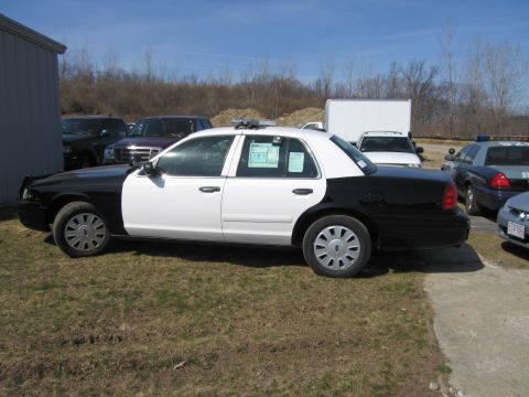 1991 Ford LTD Crown Victoria - Rear quarter view of a black-and-white Ford Crown Victoria police sedan with roof light bar and window paperwork, parked outdoors.