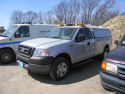 1991 Ford LTD Crown Victoria - silver Ford F-150 pickup with a bed cap marked Oxford Animal Control parks beside a white mobile command van on a lot.