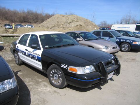 1991 Ford LTD Crown Victoria - Front three-quarter view of a black-and-white Boston University Police sedan numbered 596 with a push bar among other cars on a lot.
