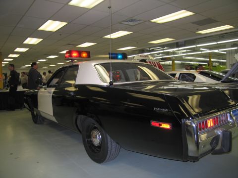 1991 Ford LTD Crown Victoria - Rear three-quarter view of a black-and-white vintage Dodge Polara police car with a roof light setup displayed indoors among other cars.