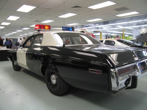 1991 Ford LTD Crown Victoria - black-and-white vintage Dodge Polara police sedan with illuminated roof lights sits on a polished indoor showroom floor.
