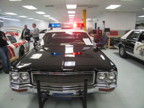 1991 Ford LTD Crown Victoria - Head-on view of a black vintage full-size police sedan with a chrome grille, roof lights and front push bar displayed in a showroom.