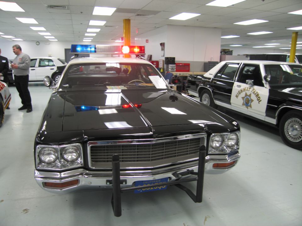 Front view of black vintage police sedan with roof lights and push bar in showroom