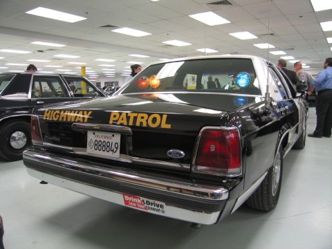 1991 Ford LTD Crown Victoria - Rear view of a black Ford Highway Patrol sedan with gold HIGHWAY PATROL lettering and California plate 888849 on a showroom floor.