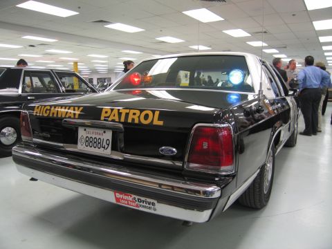 1991 Ford LTD Crown Victoria - Rear three-quarter view of a black Ford Highway Patrol sedan with a lit blue roof light and California plate 888849 displayed indoors.