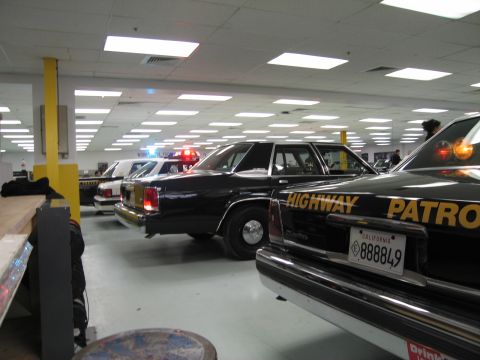 1991 Ford LTD Crown Victoria - row of dark police sedans parked indoors, foregrounded by a black Ford Highway Patrol car with plate 888849.