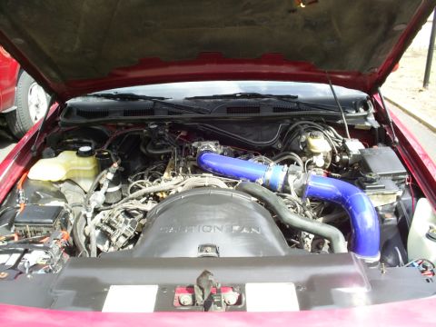 1995 Ford Crown Victoria - The engine bay of a red vehicle features prominent blue turbo piping and a 'Caution Fan' cover.