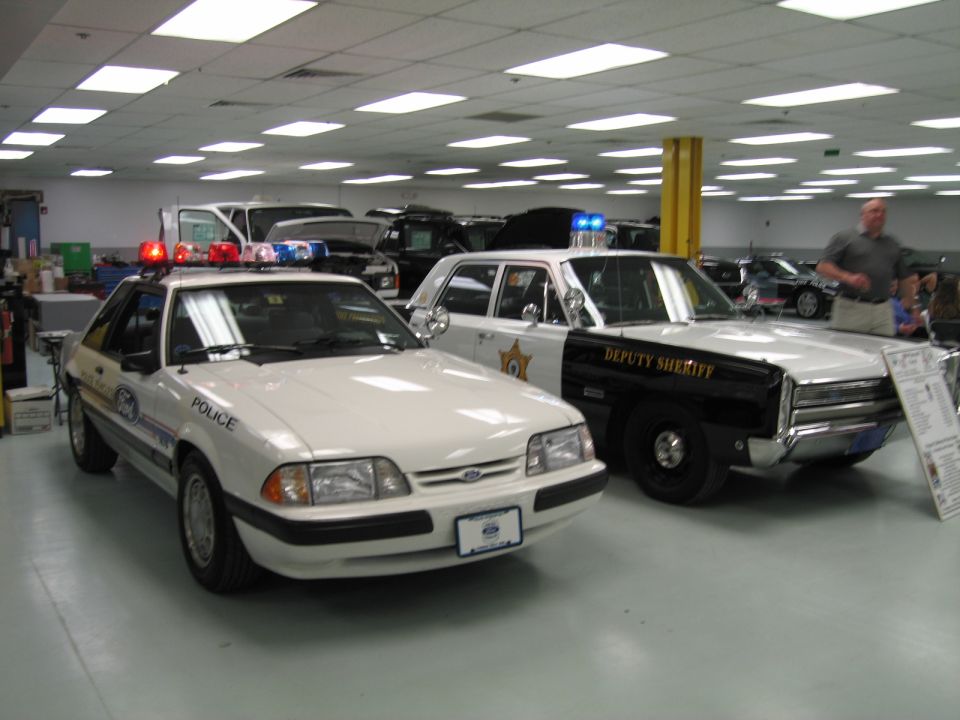 White Ford Mustang police car beside black and white Deputy Sheriff cruiser indoors