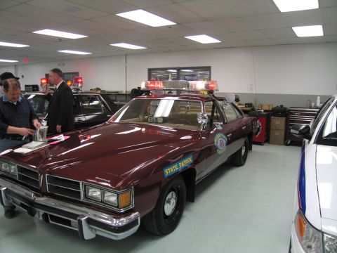 1991 Ford LTD Crown Victoria - Maroon Pontiac sedan marked State Patrol with a roof lightbar and door seal, displayed in an indoor police-car collection.
