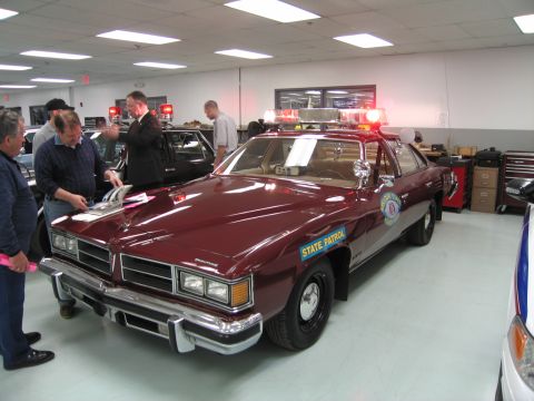 1991 Ford LTD Crown Victoria - Front three-quarter view of a maroon Pontiac State Patrol sedan with quad headlights, surrounded by visitors in a showroom.