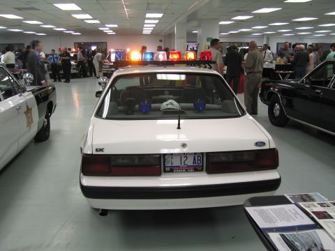 1991 Ford LTD Crown Victoria - Rear view of a white Ford LX police coupe with a lit lightbar and a plate reading 12 AB, displayed among other patrol cars.