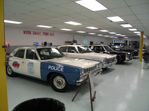 1991 Ford LTD Crown Victoria - Blue-and-white Police sedan with twin roof dome lights at the head of a row of patrol cars in an indoor museum hall.