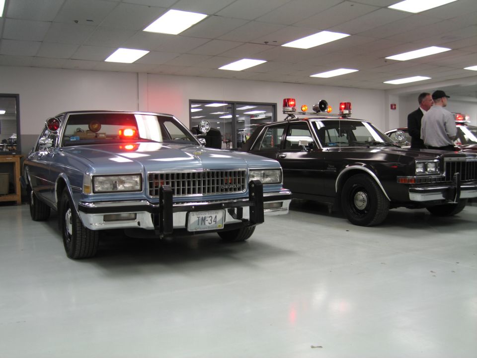 Silver-blue Chevrolet Caprice police car beside black sedan indoors