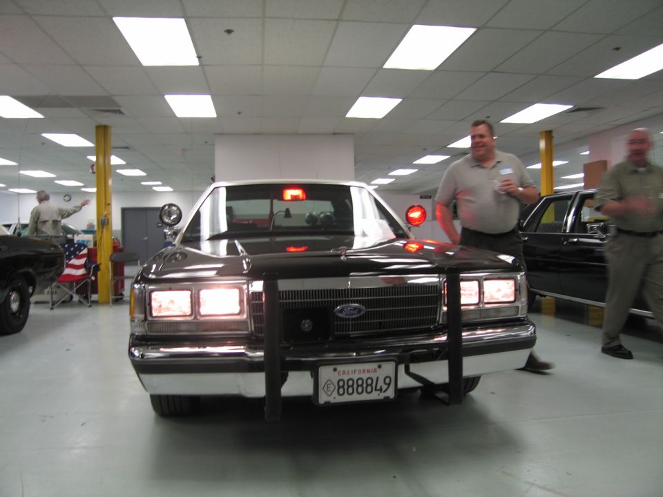 Front of black Ford sedan with push bar and California plate 888849 indoors