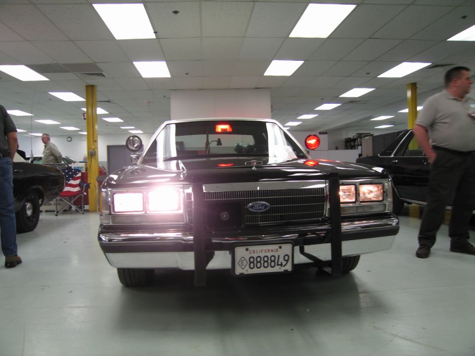 Front of black Ford sedan with push bar, California plate 888849, people nearby