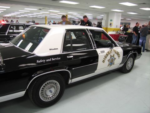 1991 Ford LTD Crown Victoria - Side view of a black-and-white Ford Highway Patrol sedan lettered Safety and Service, displayed in an indoor collection.