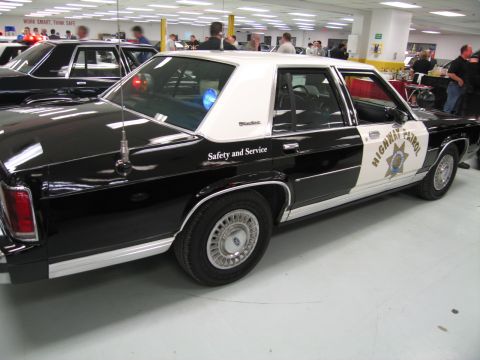 1991 Ford LTD Crown Victoria - Rear three-quarter view of a black-and-white Ford Highway Patrol sedan marked Safety and Service in an indoor display hall.