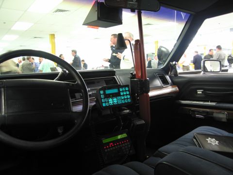 1991 Ford LTD Crown Victoria - Interior of a police cruiser with a radio keypad, handheld microphone and a wood-grain shotgun mount alongside the steering wheel.