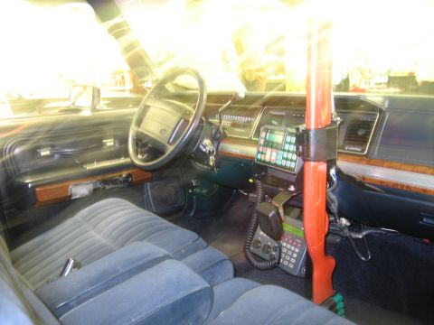 1991 Ford LTD Crown Victoria - Police car cabin showing the steering wheel, dash radio keypad, handheld microphone and a red vertical shotgun mount.