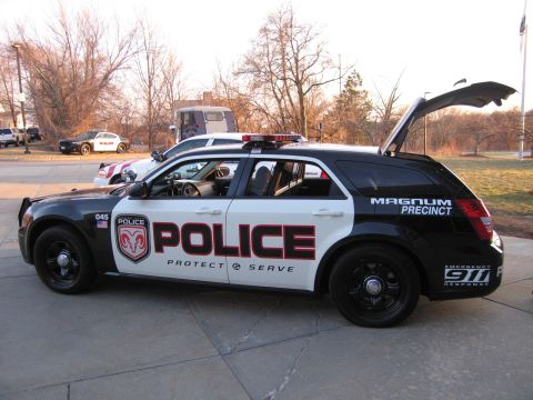 1991 Ford LTD Crown Victoria - Side view of a black-and-white Dodge Magnum police station wagon lettered POLICE with rear hatch open, parked outdoors.