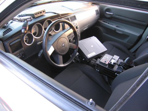 1991 Ford LTD Crown Victoria - Interior of a Dodge police vehicle with a mounted laptop, control console, and black cloth seats viewed from the passenger side.