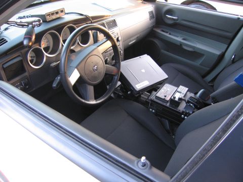 1991 Ford LTD Crown Victoria - Police vehicle interior featuring round gauges, a Dodge steering wheel, and a laptop mounted on the center console between the seats.