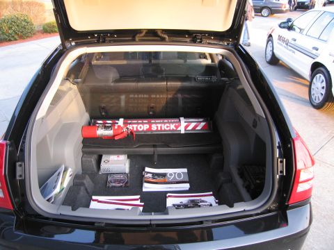 1991 Ford LTD Crown Victoria - Open rear cargo area of a black station wagon holding a red Stop Stick spike device, brochures, and equipment on the carpeted floor.