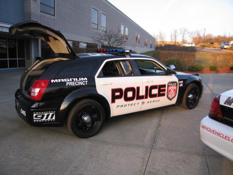 1991 Ford LTD Crown Victoria - Driver-side view of a black and white police Dodge Magnum wagon lettered POLICE Protect & Serve with a Ram-head shield emblem and roof ligh…