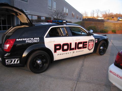 1991 Ford LTD Crown Victoria - Side profile of a black and white police Dodge Magnum wagon marked POLICE and Magnum Precinct, parked on pavement outside a brick building.