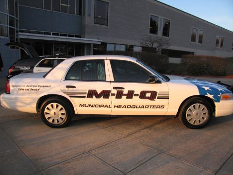 1991 Ford LTD Crown Victoria - White Ford Crown Victoria sedan decorated with M-H-Q Municipal Headquarters graphics and a flag motif on the rear quarter.
