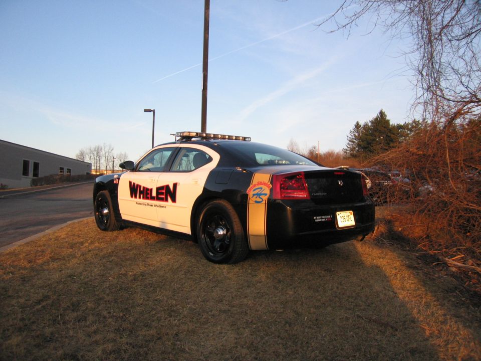 Rear three-quarter of black and white WHELEN Dodge Charger with gold stripe
