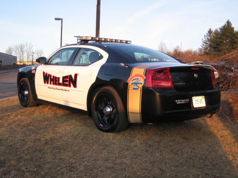 1991 Ford LTD Crown Victoria - Rear three-quarter view of a black and white Dodge Charger with WHELEN graphics, a gold stripe, and roof light bar parked on grass.