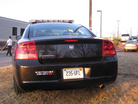 1991 Ford LTD Crown Victoria - Rear view of a black Dodge Charger with a roof light bar, a humorous bumper sticker, and a Connecticut plate reading 235 UFL.