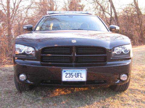 1991 Ford LTD Crown Victoria - Head-on front view of a black Dodge Charger with bright halo headlights, roof light bar, and a Connecticut plate reading 235 UFL.