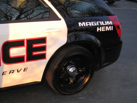 1991 Ford LTD Crown Victoria - Rear-quarter close-up of a black-and-white police wagon with a black steel wheel, red taillight, and MAGNUM HEMI badging.