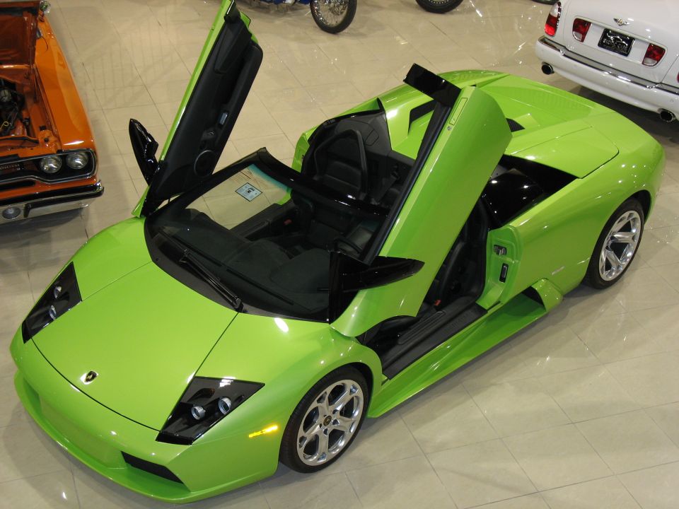 Green Lamborghini Murcielago roadster with doors up in a showroom