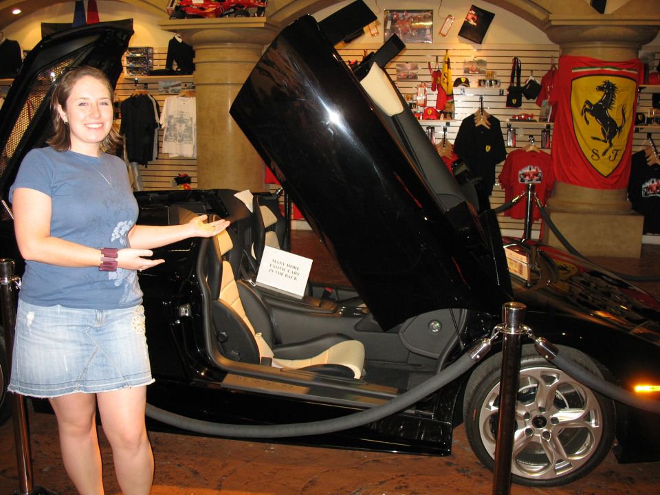 Black sports car with butterfly doors open, tan interior, and a woman standing next to it