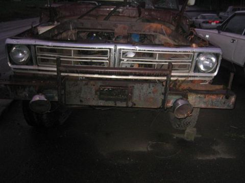 1986 Ford Bronco - The front of a heavily rusted truck is shown, with its hood open and grille exposed. Other vehicles are visible in the background.