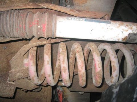 1986 Ford Bronco - Front suspension part, likely a shock absorber and coil spring, shows significant rust.