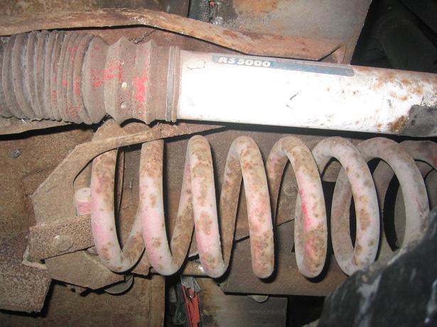 Close-up of a rusty coil spring and white shock absorber labeled RS 5000