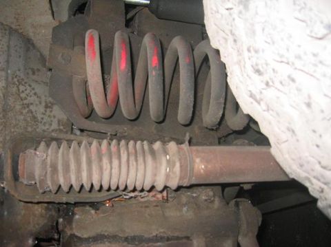 1986 Ford Bronco - Detail of a vehicle's front suspension system, showing a coil spring and a protective boot over the axle.