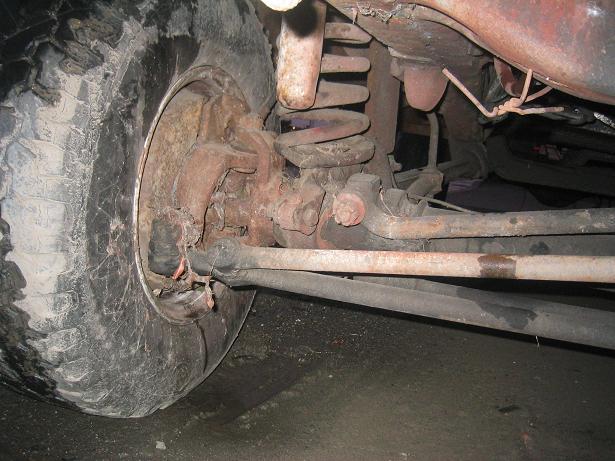 Close-up of a vehicle's front tire and suspension components, showing rust and wear