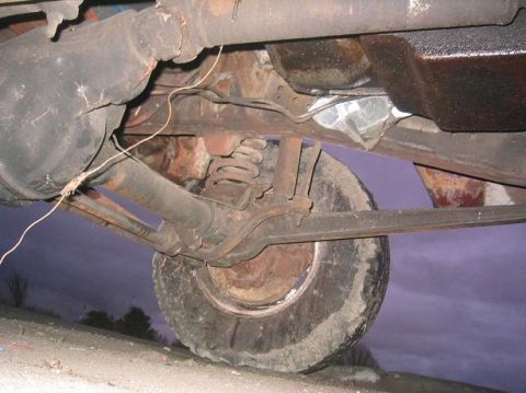 1986 Ford Bronco - The underside of an old vehicle reveals its rear axle and suspension components, with a dark sky in the background.