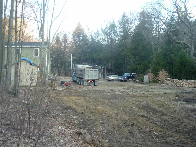 Dump truck, sedan, and SUV parked in a muddy yard next to a house and trees