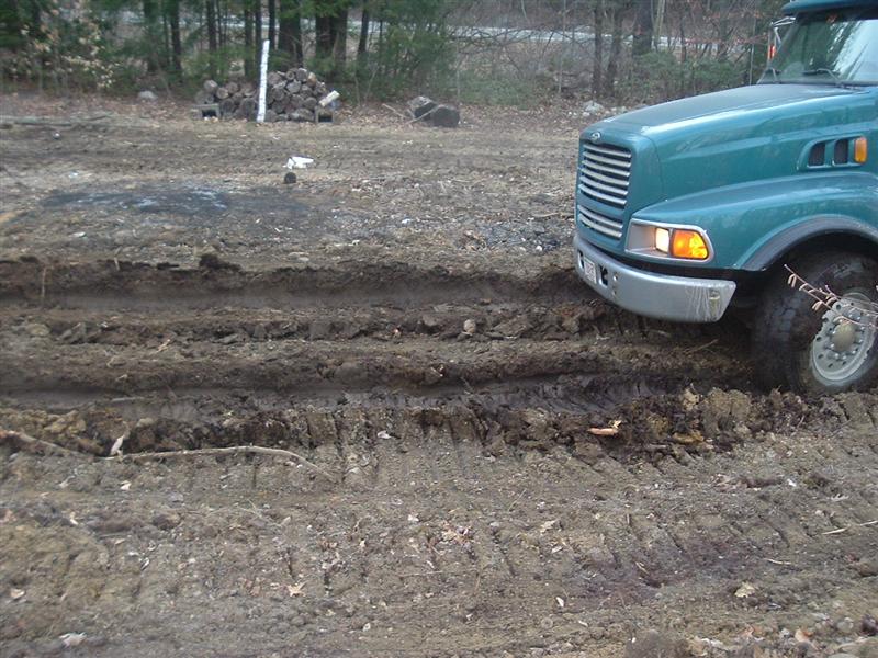 Teal semi-truck front view stuck in muddy terrain with tire tracks