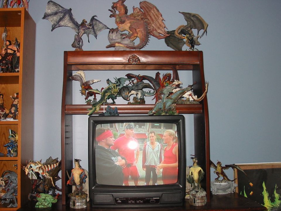 Shelf filled with dragon figurines above a television showing four people